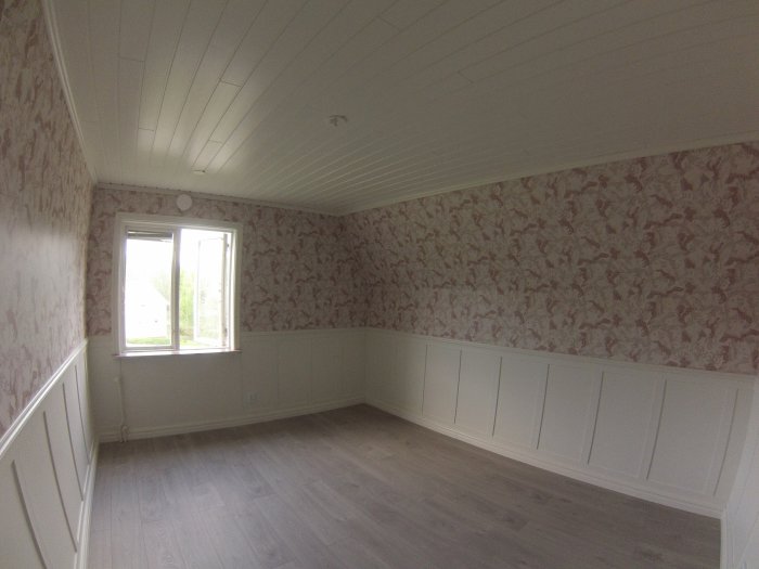 Nyligen renoverat rum med trägolv, väggpanel och tapeter redo för möblering.