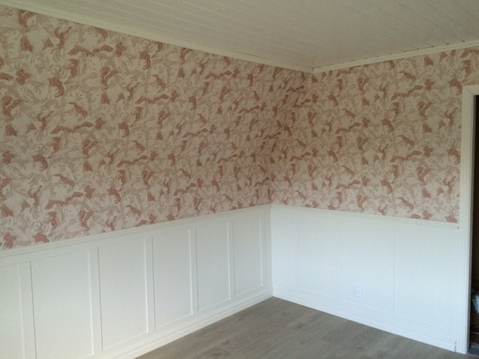 Nästan färdigrenoverat rum med vit panel och tapet med blommönster, tomma väggar redo för inredning.