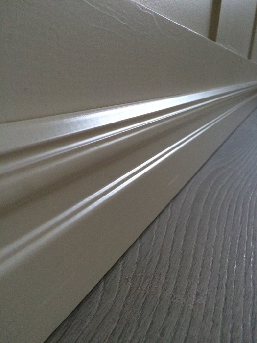 Närbild på nyligen installerad vit fönsterbräda ovanför grått golv, med reflektion av ljus.