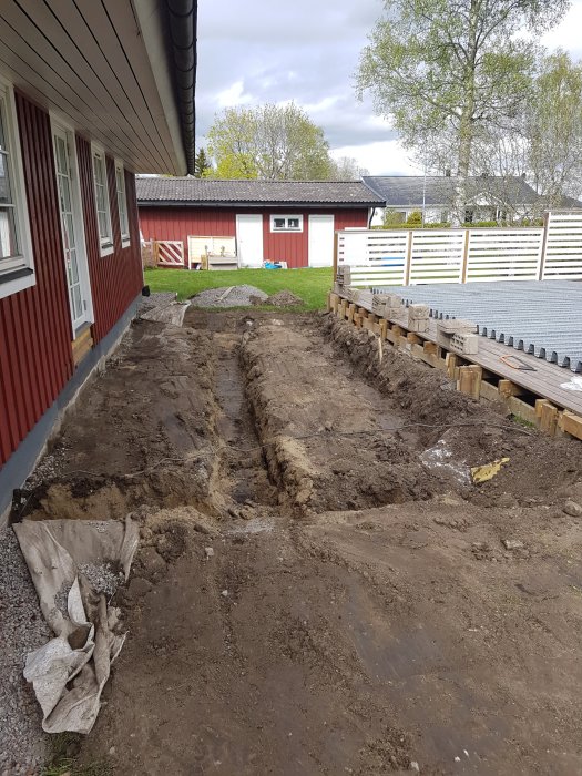 Uppgrävd mark för grundläggning av inglasat uterum bredvid hus.