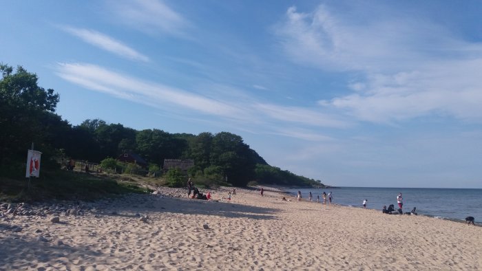 Solig sandstrand med badande människor och en klarblå himmel.