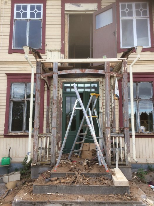 Renovering av farstukvist med räddade stolpar och snickarglädje, trästege framför, byggbråte på marken.