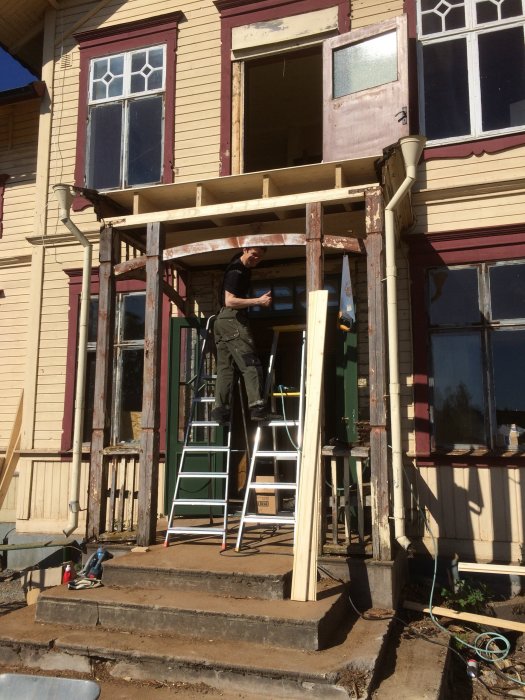 Renovering av farstukvist med räddade stolpar och nytt bjälklag, person målar stolpe på stege.