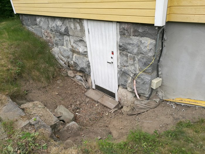 Källarentré med hål i marken, slarvigt dragen fiberkabel och synlig filterduk vid gammal husgrund.