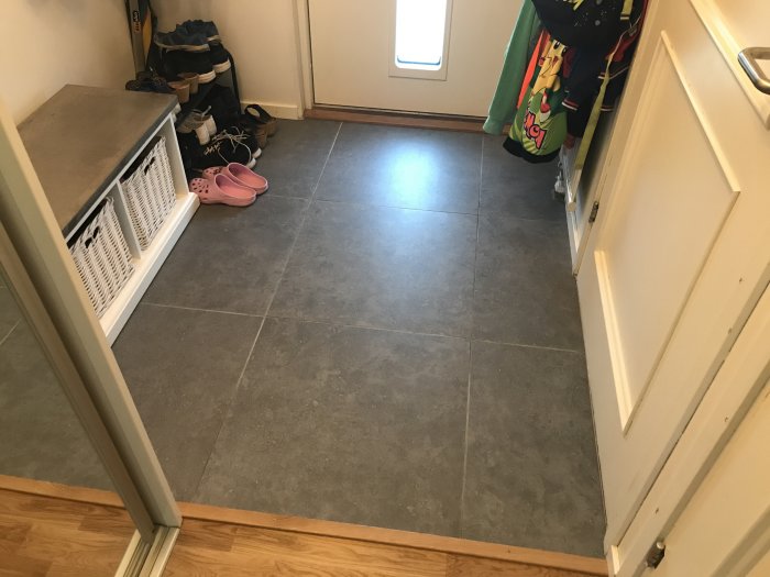Nyrenoverad hall med grå klinkergolv, skor längs väggen och hängande jackor.