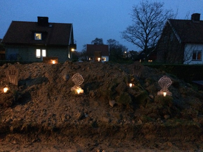 Halloween-dekoration med gravgårdstema, falska gravstenar och ljus i kvällsbelysning framför hus.