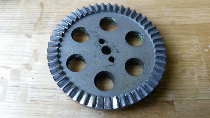 Grått kugghjul med centralt hål och fyra mindre hål omgiven av tänder, reservdel till en häcksax.