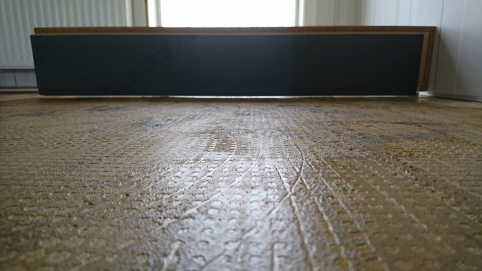 Ojämnt undergolv med gammal heltäckningsmatta och synliga avtryck, samt nytt laminatgolv i förgrunden.