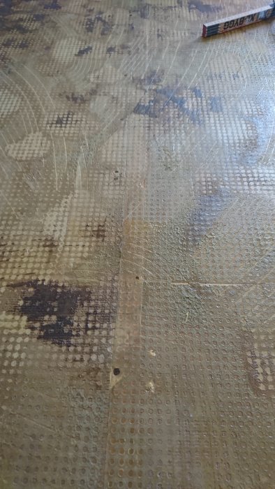 Ojämnt undergolv med rester av lim och avtryck från gammal heltäckningsmatta i ett hus byggt 1973.