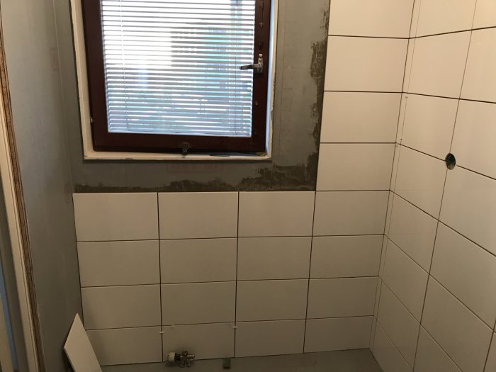 Renovering av badrum med halvt kaklade väggar och en hörnhylla monterad.