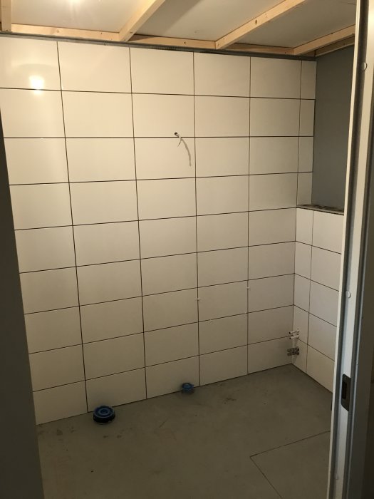 Nyinstallerade vita kakelplattor på vägg i ett pågående renoveringsprojekt i ett badrum.