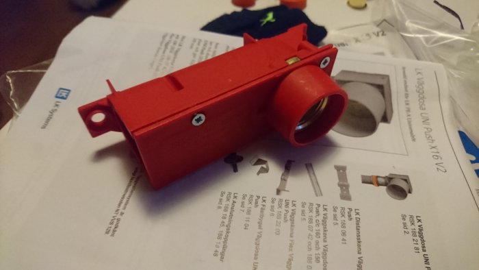 Röd väggdosa med G15-gänga och tillhörande rörkopplingsdetaljer på ett bord.