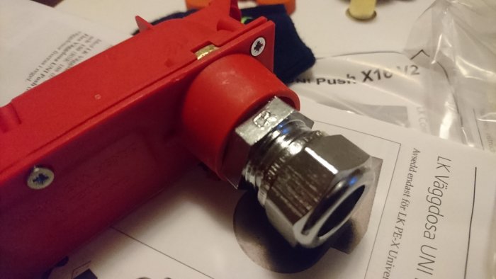 Röd väggdosa med påmonterad metallkoppling och instruktionsblad i bakgrunden.