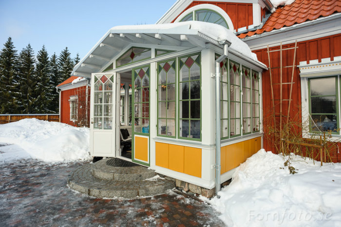 Isolerad farstu med glaspartier och golvvärme kopplad till rött hus omgiven av snö.