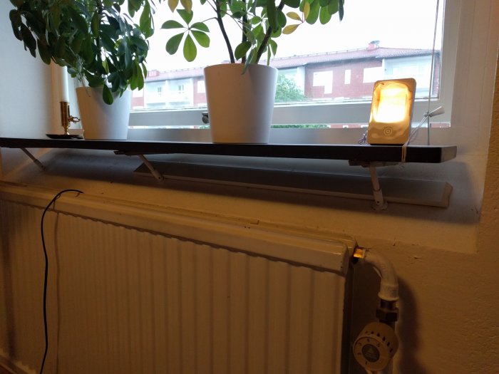 Inomhusvy av fönsterbräda ovanför en radiator med växter och en bärbar lampa, i fråga om fästning på PVC-fönster.