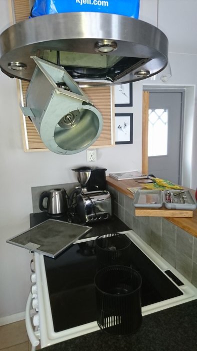 Kök med öppen köksfläkt hängandes i kabeln över spishäll, fettfilter och delar på bänken.