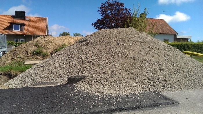 Stor grushög framför ett hus med en annan sandhög i bakgrunden under klar himmel.