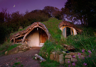 Ett hus inspirerat av Hobbiton med en rund dörr, inbyggt i en kulle, omgivet av grönska och stensteg.
