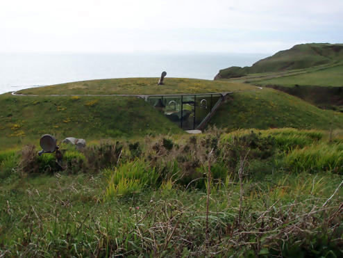 Jordhus integrerat i gröna kullar med hav i bakgrunden, känd som "Malator" i Pembrokeshire, Wales.