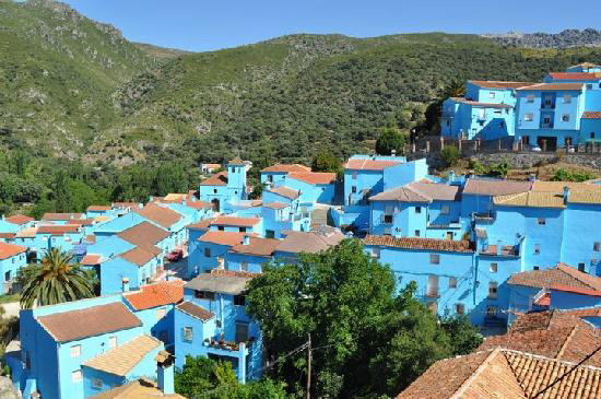 Vy över den smurfblå byn Juzcar i Spanien med blåmålade hus omgivna av grönska.