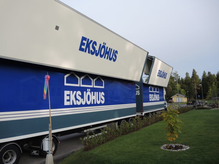Lastbilar med Eksjöhus-logotyper parkerade på en gräsmatta under husstommeresning.