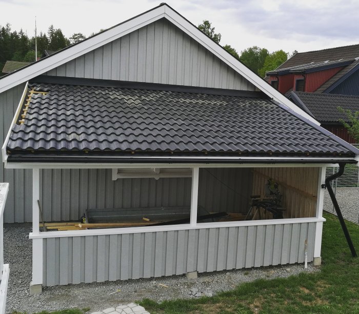 Nyinstallerad plåt mellan en gråmålad carport och husets tegelliknande svarta tak.