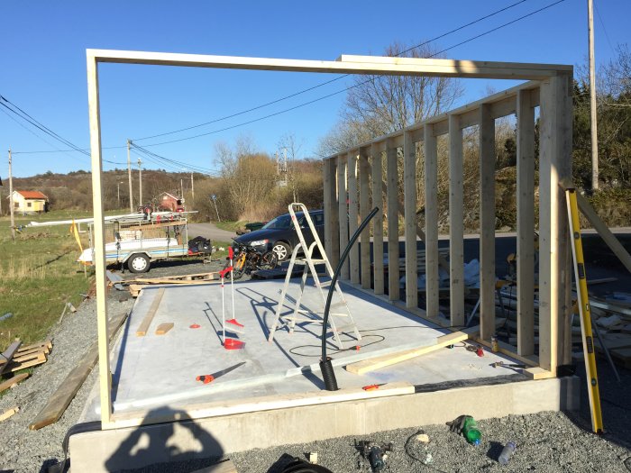 Påbörjad stomme för en byggnad med upprättade träreglar och horisontella stöd på en betonggrund utomhus.