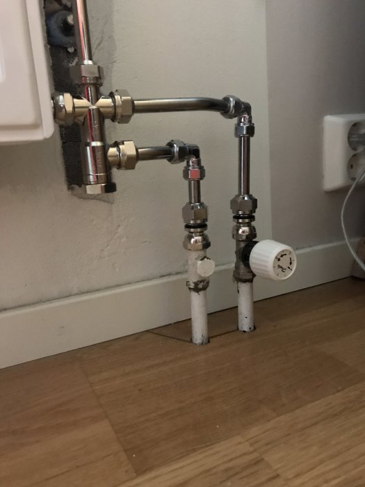 Radiatorrör och termostat vid golv med synliga kopplingar och en gammal termostat kvar.