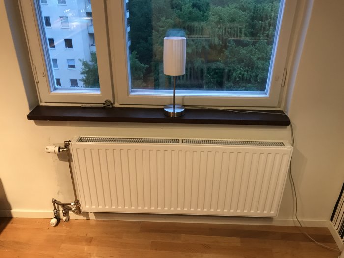 Nyinstallerad vit radiator under ett fönster, ej centrerad och nära fönsterbrädan, med gamla termostater kvar.