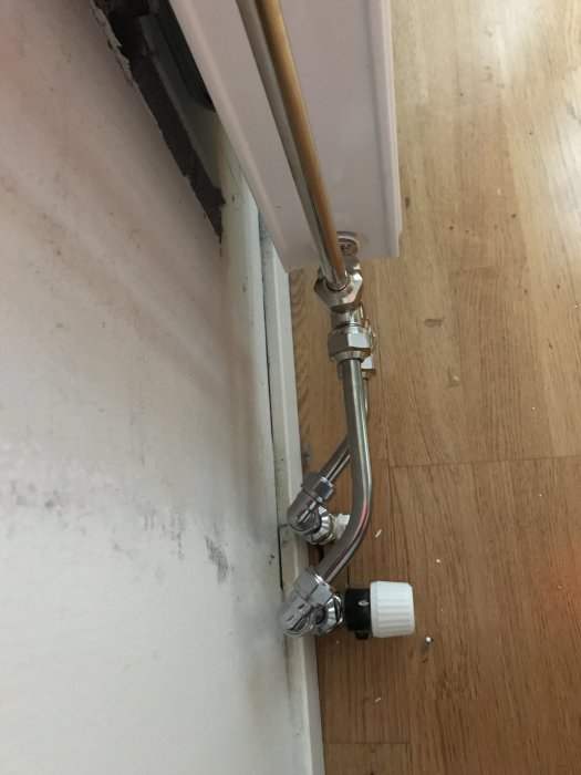 Nyinstallerad radiator med rör och en ny termostat som inte är centrerad under fönstret.