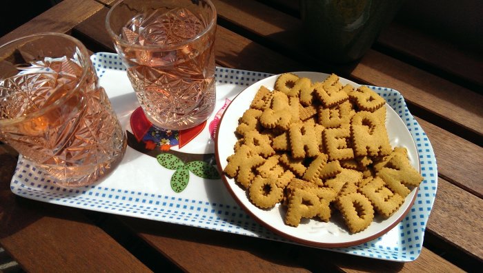 Kakor formade som bokstäver för att stava 'köp hem' på en tallrik bredvid två glas rosévin.