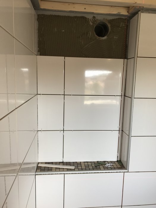 Nytt kakel är installerat på vägg med ofärdig del upptill och en nisch med mosaik.