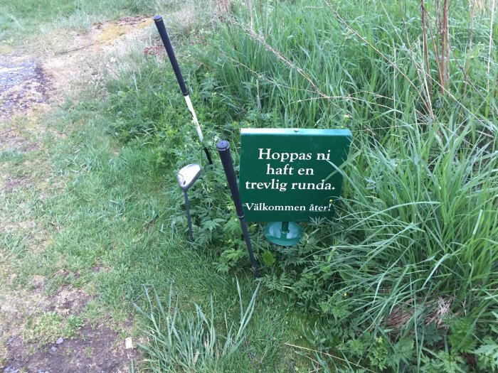 Skylt med texten "Hoppas ni haft en trevlig runda. Välkommen åter!" bredvid en bortslängd golfklubba i gräset.