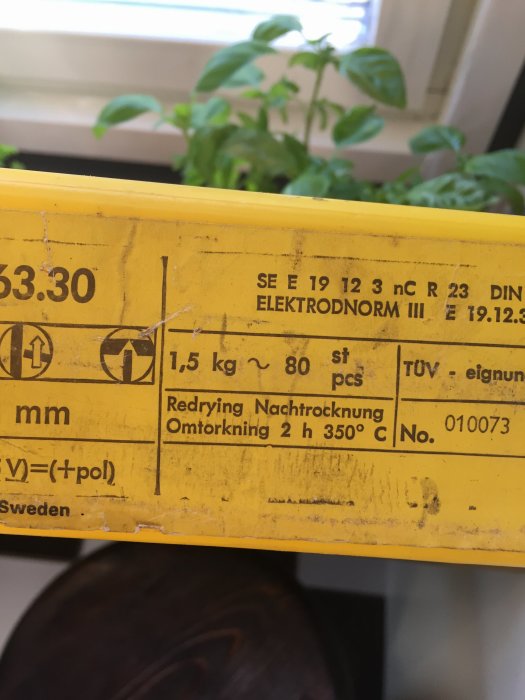 Etikett på förpackning med instruktion för omvärme till 350 grader Celsius i två timmar, med växt i bakgrunden.