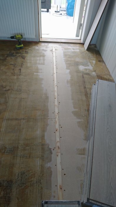Halvslipat trägolv med tydlig gräns mellan bearbetad och obehandlad yta, slipmaskin och byggmaterial i bakgrunden.