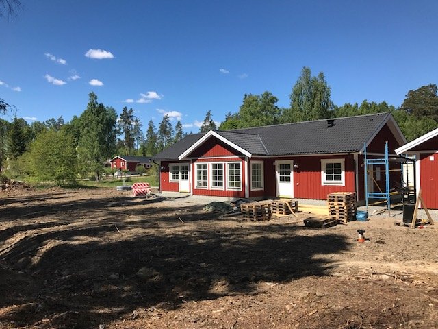 Nybyggt rött hus med vita fönsterkarmar och nymålad entré under konstruktion, ojämn mark framför.