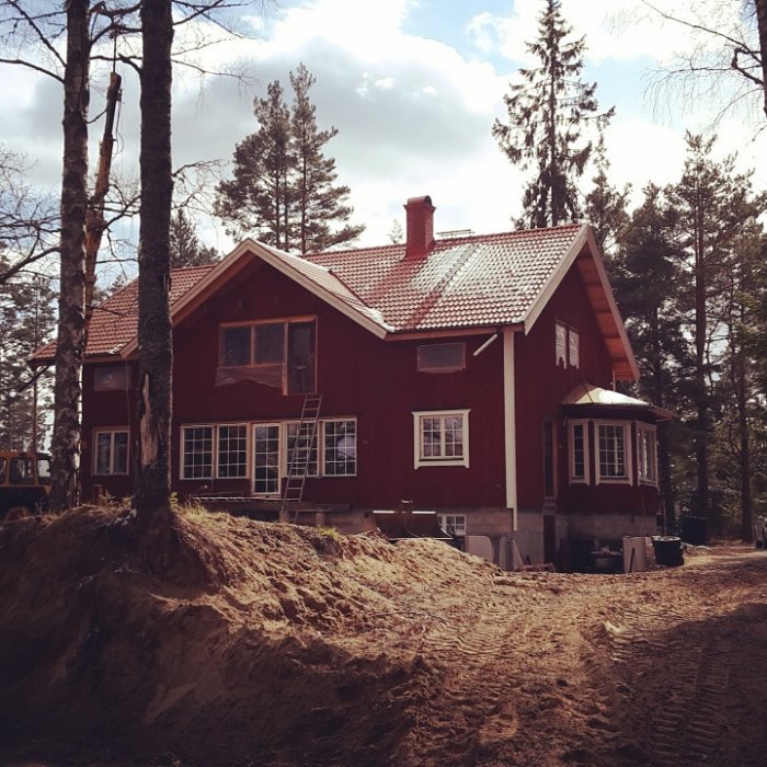 Rödmålat hus under konstruktion med synlig källardel och omgivande skog.