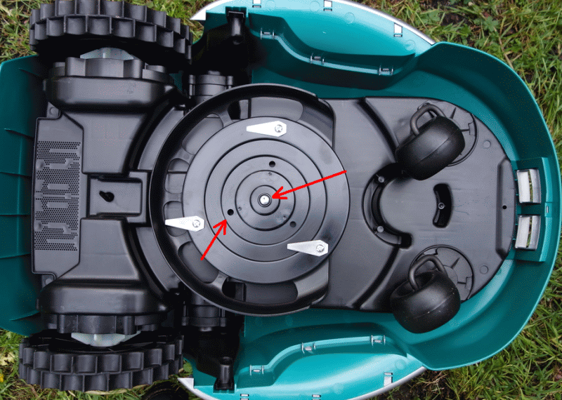 Undersidan av en robotgräsklippare med synlig central skruv och markerade skruvhål där bladen är monterade.