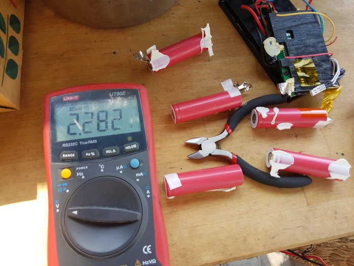 Öppnat lithium-batteripaket med elektronik och mätinstrument som visar spänning på 2.82V, åtföljt av lösdetaljer och verktyg.