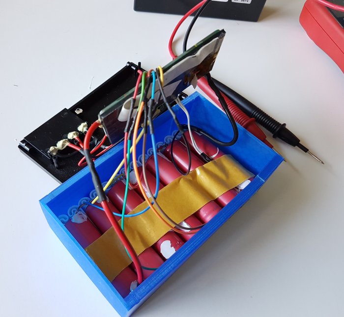 Öppnat batteripaket med upplödda lithiumceller och elektronik, omgivet av verktyg och kabeldragning.