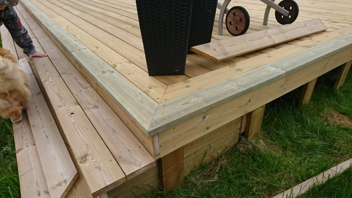 Hörn på trädäck bredvid pool med renkapade plankor och en svart planteringskruka uppe på däcket.