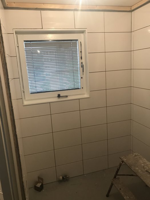 Renoverad fönster med persienn i kaklat rum, beslag återmonterade, förberedelse för golvinstallation.