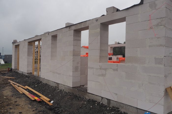 Nybyggd vägg av gråa betongblock med öppningar för fönster eller dörrar på en byggarbetsplats.