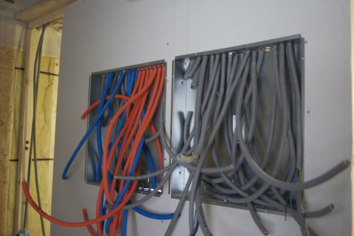 Elektriska slangar i olika färger som sticker ut ur två infällda elskåp i en vägg under konstruktion.