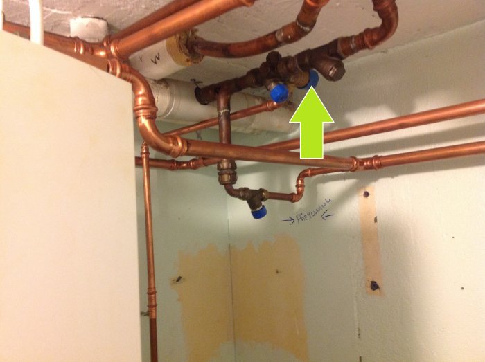 VVS-installation med kopparledningar och blå säkerhetsventil markerad med en grön pil.