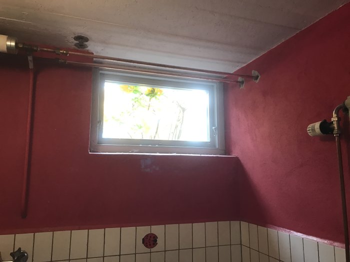 Nyinstallation av vattenrör längs med rosa vägg och tak över kakel i badrum, med synligt källarfönster.