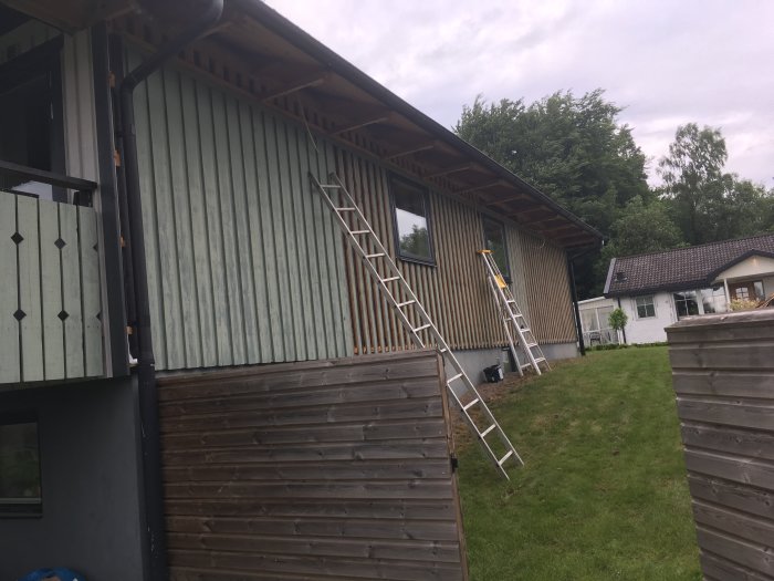 Husfasad under renovering med första lagret av träpanel uppsatt och en stege lutad mot huset.