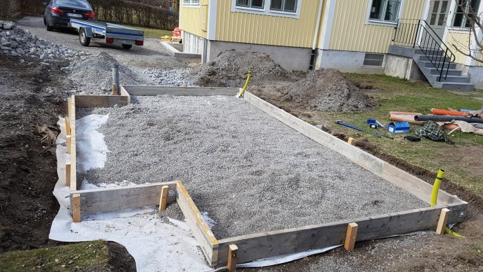 Nygrusad yta för förrådsplatta framför hus med verktyg och släpkärra.