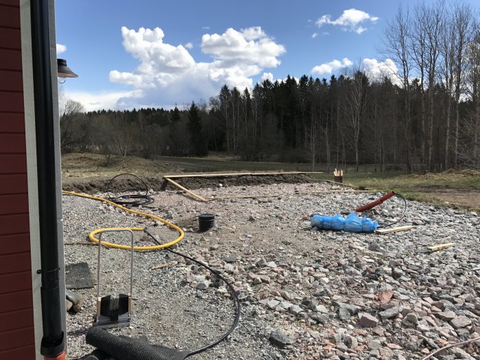 Förberedelser för bygge av en stor altan med grusgrund, ramar av trä och byggmaterial synliga på tomten.