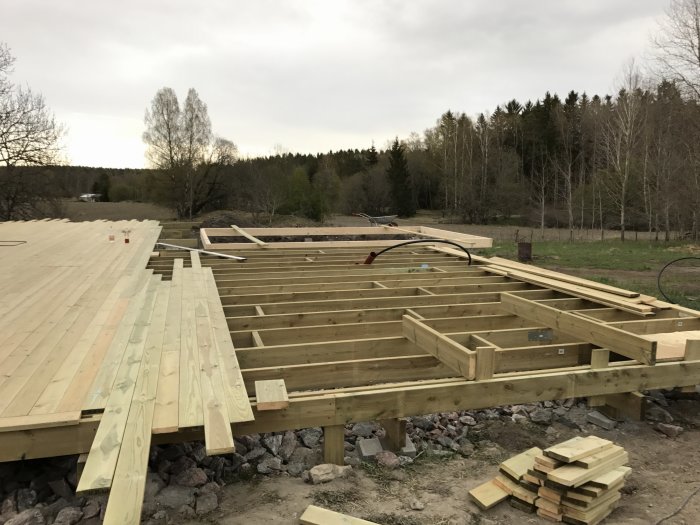 Byggställning för däck med träram och plankor mot naturlig bakgrund.